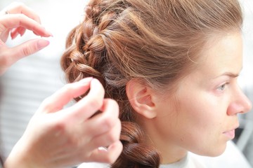 Fototapeta premium styling curls and weaving French braid on long hair in salon