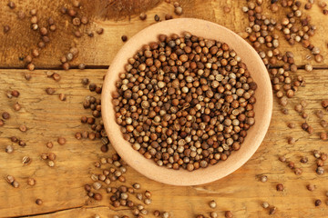 Heap coriander seeds in bowl on wooden background close-up
