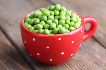 Green peas in red cup on wooden background