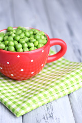 Green peas in red cup on wooden background