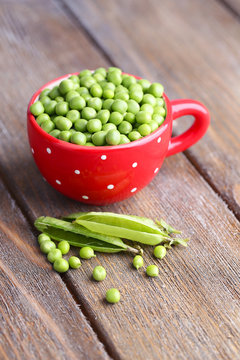 Green peas in red cup on wooden background