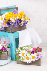 Beautiful flowers in crates on small chair on light background