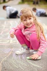 Cute little girl drawing with chalk outdoors