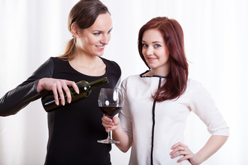 Young woman pouring wine for her friend