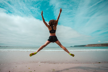 Young woman doing star jumps on the beach - 65969144