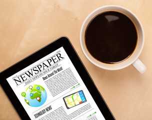 Tablet pc shows news on screen with a cup of coffee on a desk