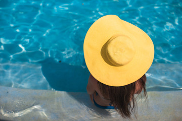 Young woman in yellow hat relaxing at swimming pool