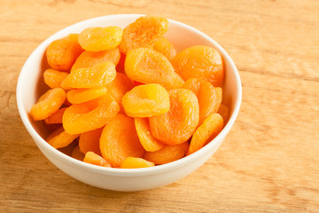Bowl of dried apricots on wooden table background.