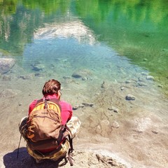 uomo con zaino di spalle che si rinfresca su un lago alpino