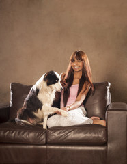 Young beautiful indian woman sitting on couch playing with dog