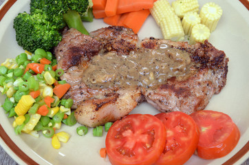 Grilled steaks, baked potatoes and vegetables on white plate on