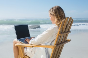 Gorgeous blonde sitting on deck chair using laptop on beach
