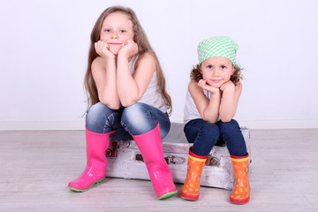 Beautiful small girls sitting on suitcase on wall background