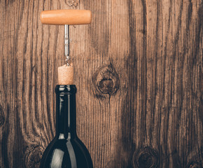 Bottle of wine and corkscrew on wooden background