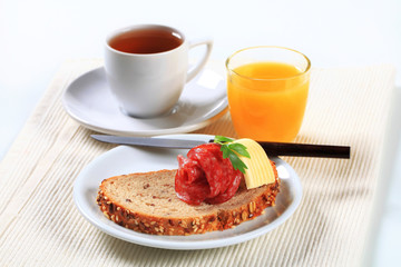 Bread with salami, cup of tea and orange juice