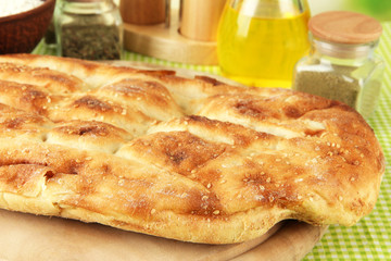 Pita bread on wooden stand with spices on tablecloth close up