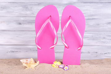 Bright flip-flops on sand, on wooden background