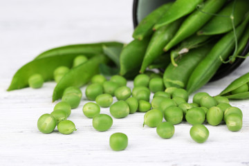 Fresh green peas in metal cup on wooden table