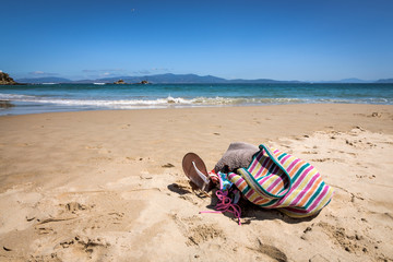 Purse, sunglasses, slippers, and towel at the beach