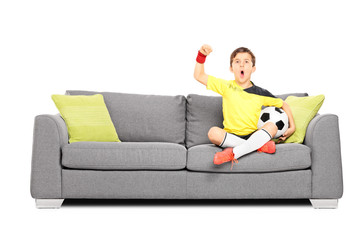 Kid cheering and holding football seated on sofa