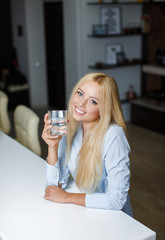 Beautiful young woman holds a glass with water on kitchen