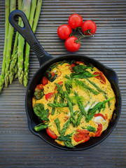 Omelette with asparagus and tomato on frying pan
