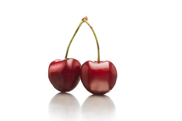 Two ripe red shiny cherries with connected stems