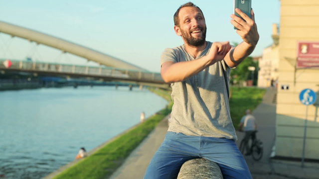 Man taking selfie photo with cellphone, sitting on the wall 