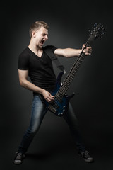 young male musician playing a six-string bass guitar isolated on