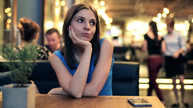 Young pensive woman sitting alone in restaurant