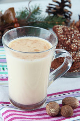 Cup of eggnog with cookie and fir branches on table close up
