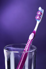 Toothbrush in glass on purple background