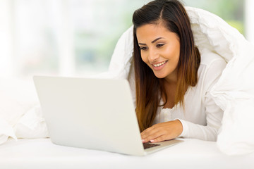 woman using laptop computer while lying on her bed