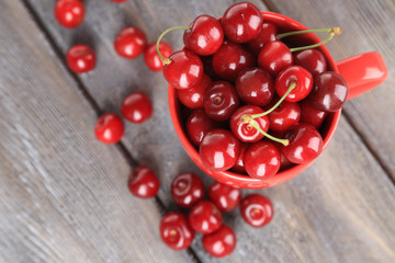 Sweet cherries in mug on wooden background