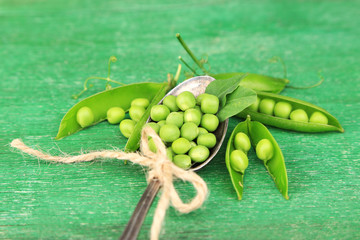 Fresh green peas in spoon on wooden table