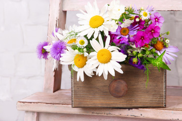 Beautiful flowers in crate on small ladder on light background