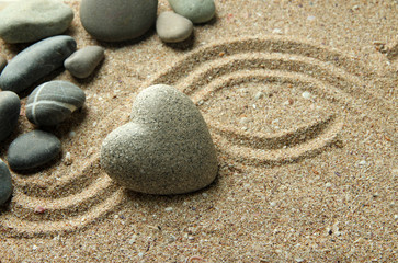 Fototapeta na wymiar Grey zen stone in shape of heart, on sand background