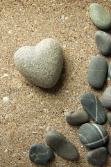 Fototapeta na wymiar Grey stone in shape of heart, on sand background