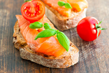 Salmon sandwich on wooden table with tomato