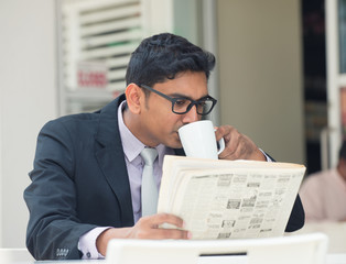 indian business male with newspaper and coffee at a cafe