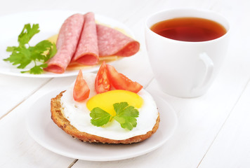 Sandwich with fried egg, tomato slices and tea