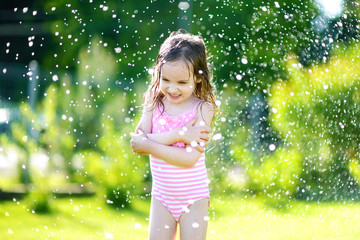 Girl running though a sprinkler in a backyard