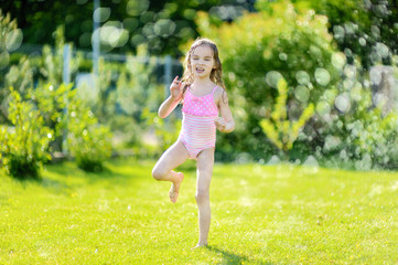Obraz premium Girl running though a sprinkler in a backyard