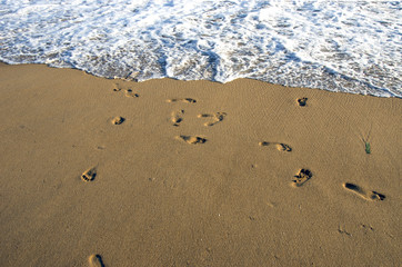 Fototapeta na wymiar barefoot footsteps on ocean beach sand and wave
