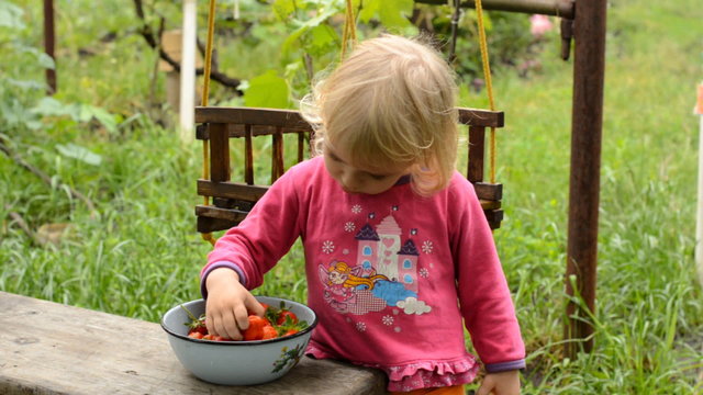 Cute Little Girl Eating Strawberry in Green Garden