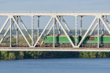 green electric locomotive passing the bridge over the river in s