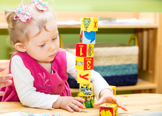 Little child girl playing with toy letter and number blocks