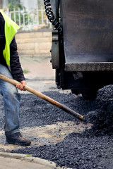 Worker manually effusing asphalt with paving machine