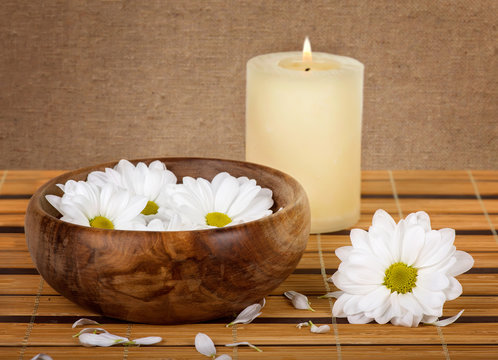 Spa decoration with candle and daisies on a bamboo mat