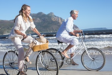Obraz premium Smiling couple riding their bikes on the beach